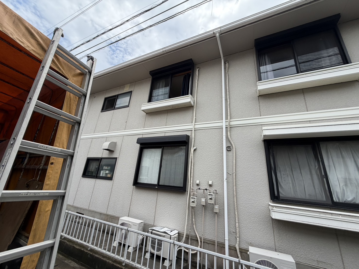 武岡の住宅街での室外機設置。はしごを使った屋外作業の様子